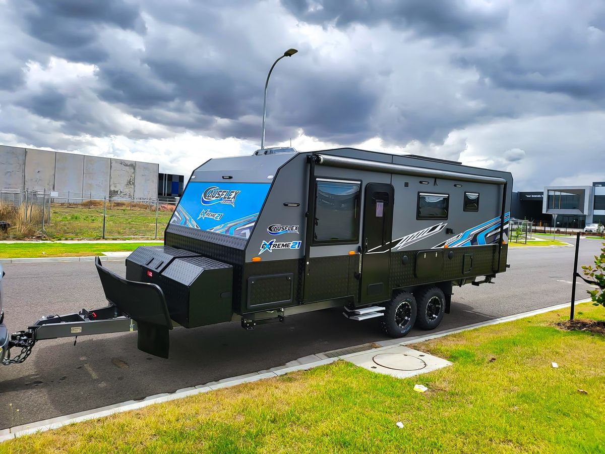 Ausflex Xtreme 21 in olive with blue graphics, front three-quarter under a stormy sky