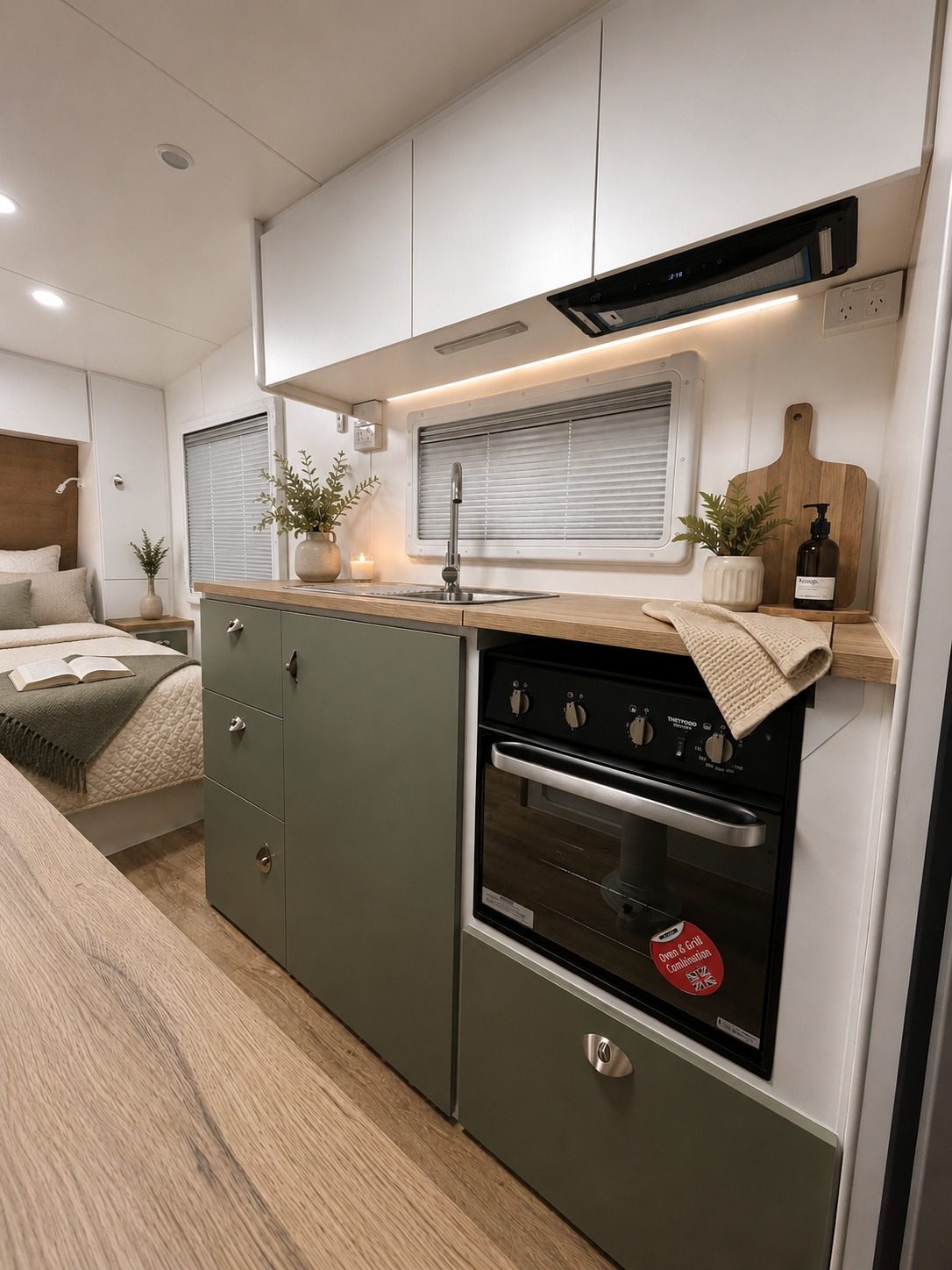 Olive green kitchen with timber benchtop and oven, bed beyond